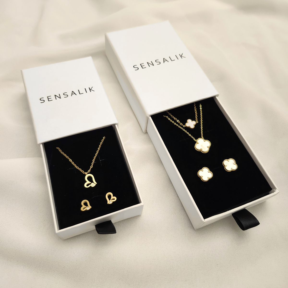 Gift Box in two sizes with white Sensalik sleeves and black inserts, displaying heart and white clover necklace-and-earring sets.