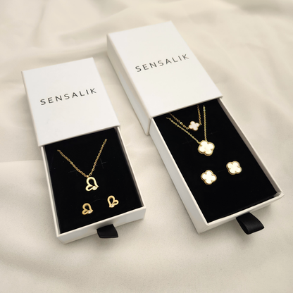Gift Box in two sizes with white Sensalik sleeves and black inserts, displaying heart and white clover necklace-and-earring sets.