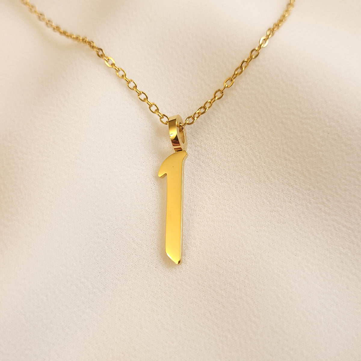 Gold-tone Arabic Initial Necklace with the letter Alif (ا) on cream fabric.

