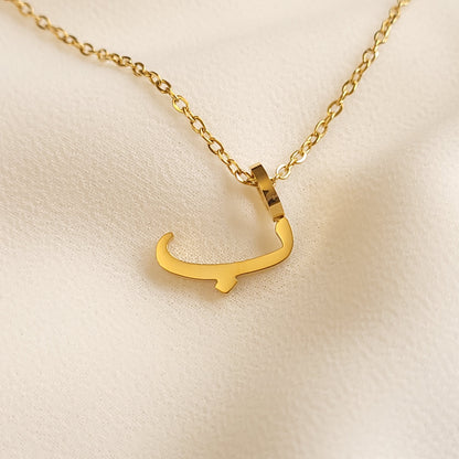 Gold-tone Arabic Initial Necklace with the letter Baa (ب) on cream fabric.
