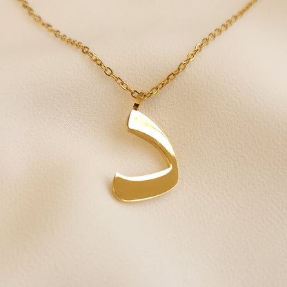 Gold-tone Arabic Initial Necklace with the letter Dal (د) on cream fabric.
