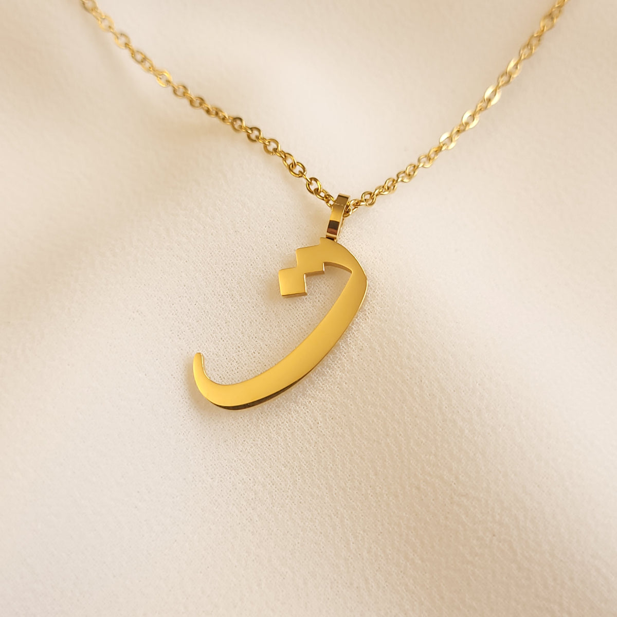 Gold-tone Arabic Initial Necklace with the letter Taa (ت) on cream fabric.
