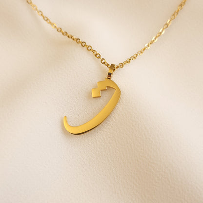 Gold-tone Arabic Initial Necklace with the letter Taa (ت) on cream fabric.
