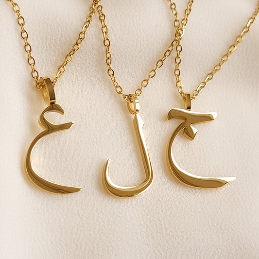 Gold-tone Arabic Initial Necklaces featuring Ain (ع), Lam (ل) and Jeem (ج) pendants on fine link chains.
