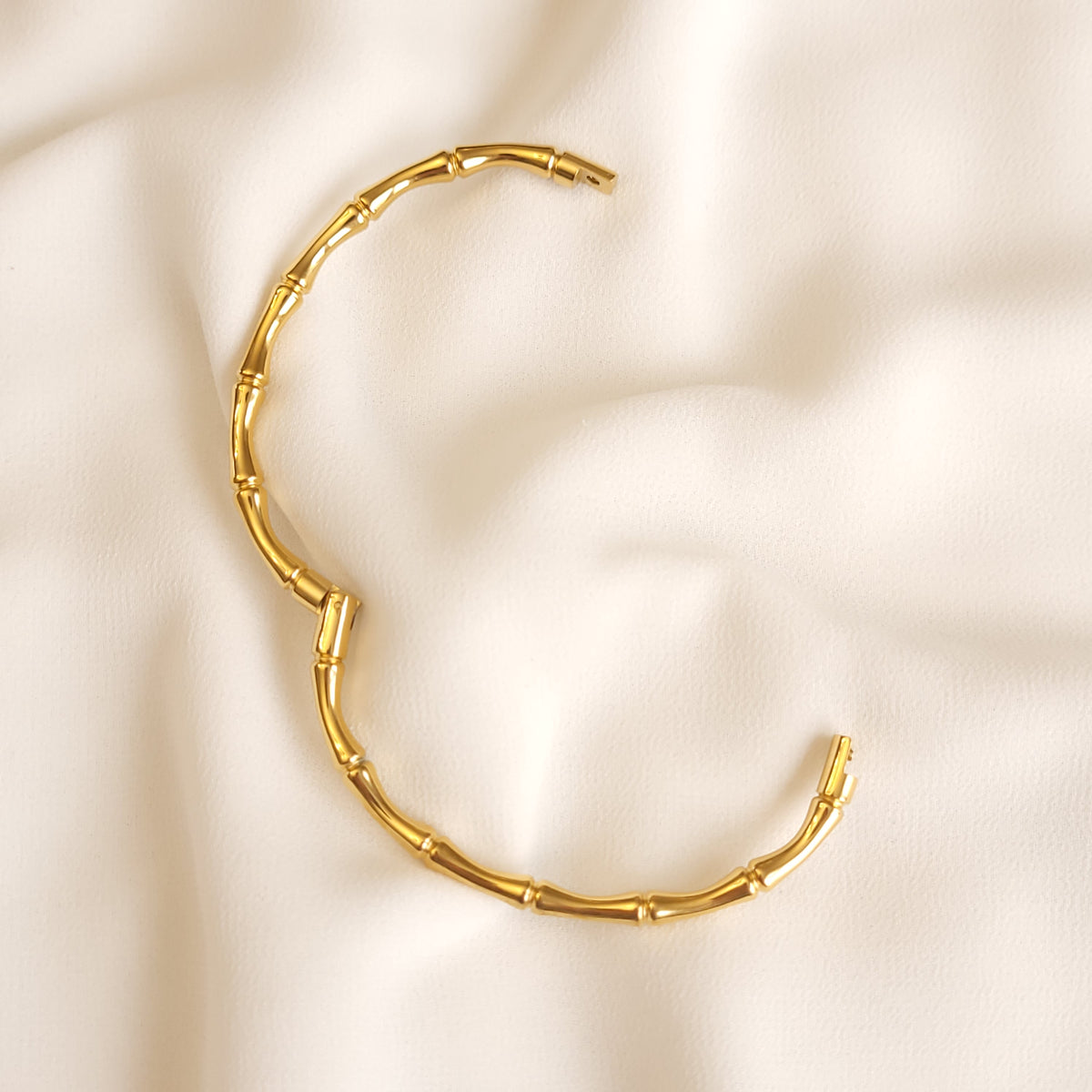 Gold-tone Bamboo Inspired Bangle opened to show its hinge and clasp on cream fabric.
