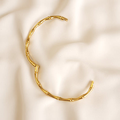 Gold-tone Bamboo Inspired Bangle opened to show its hinge and clasp on cream fabric.
