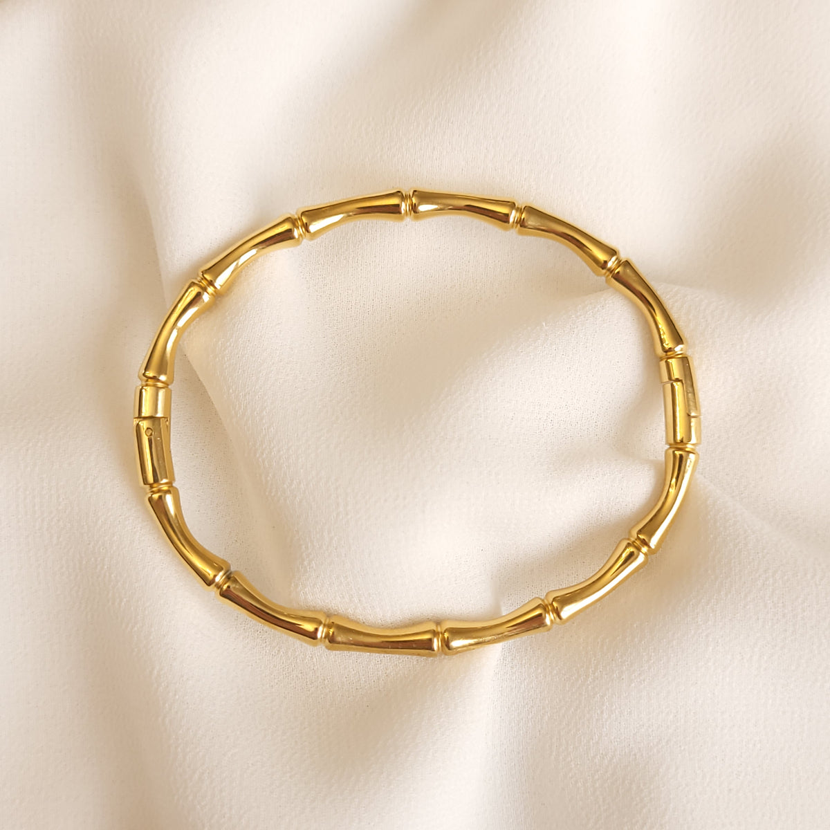 Gold-tone Bamboo Inspired Bangle with polished bamboo-shaped segments and raised joints on cream fabric.
