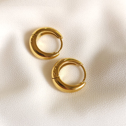 Gold-tone Basic Tapered Huggie Earrings with polished curved hoops on cream fabric.
