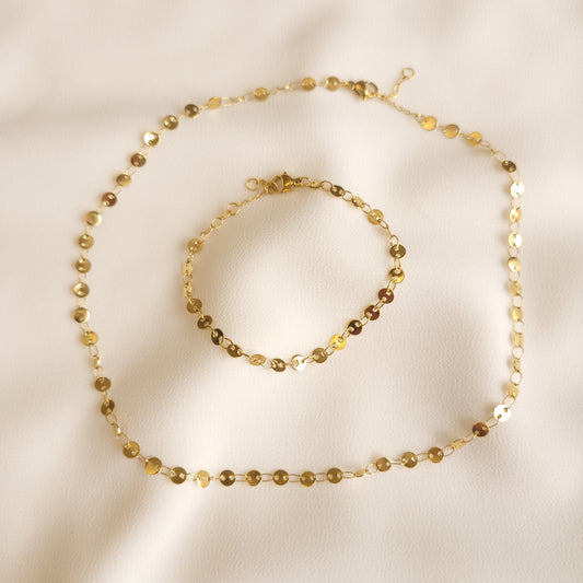 Gold-tone Coin Set with a matching necklace and bracelet featuring small polished round discs linked together on cream fabric.
