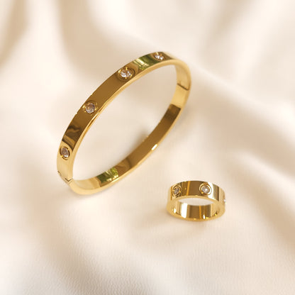 Gold-tone Crystal Stud Set featuring a polished bangle and matching ring with spaced round clear stones on cream fabric.
