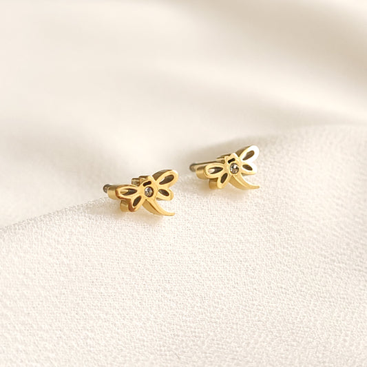 Gold-tone Dragonfly Stud Earrings with openwork wings and small clear stone accents on cream fabric.
