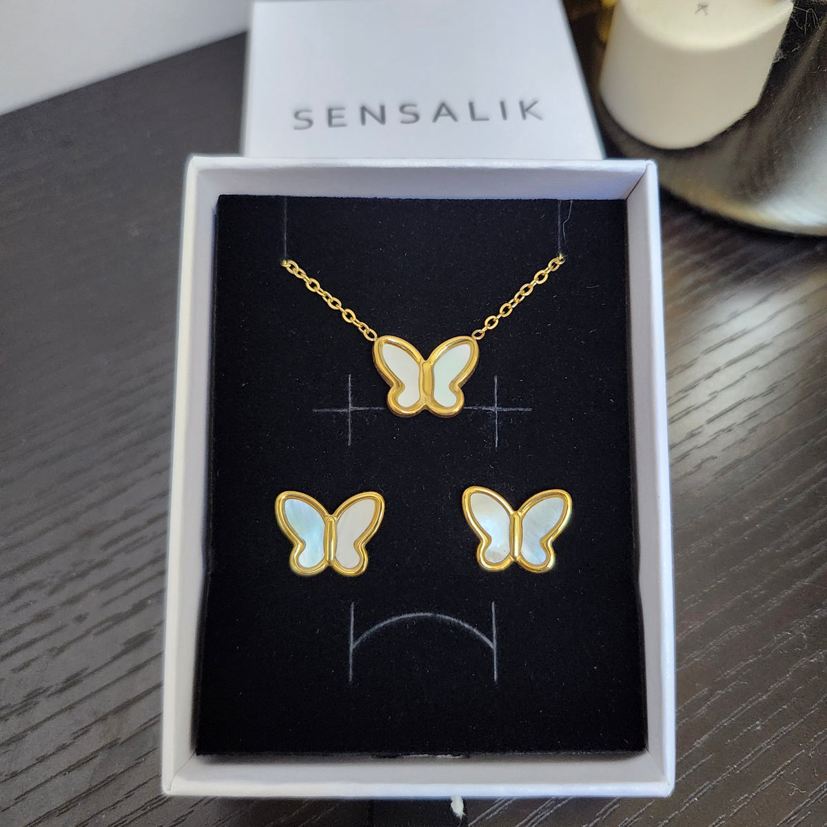 Gold-tone butterfly necklace and matching stud earrings with iridescent white wings, displayed in an open gift box.
