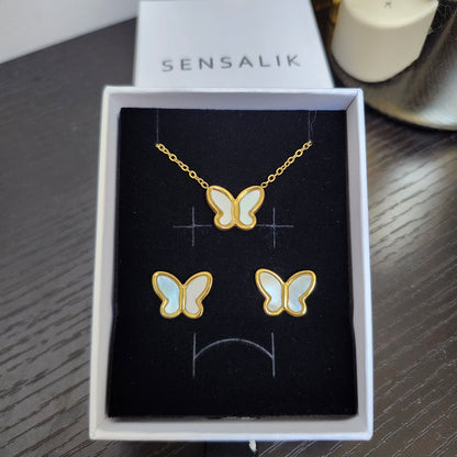 Gold-tone butterfly necklace and matching stud earrings with iridescent white wings, displayed in an open gift box.