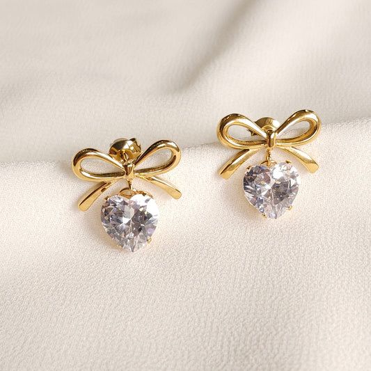 Gold Bow and Heart Earrings with polished bow studs and dangling clear heart-shaped stones.