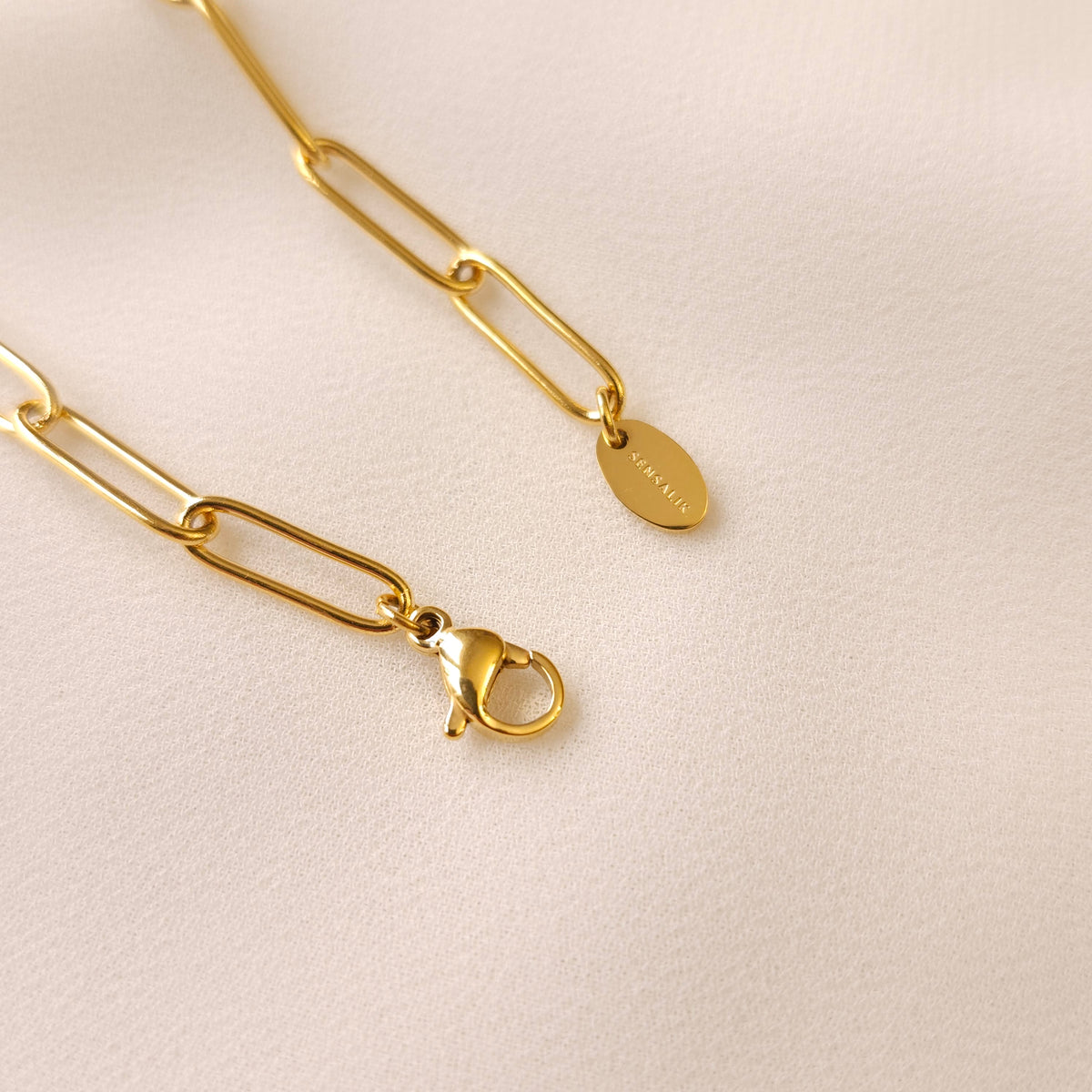 Gold Paperclip Bracelet showing its lobster clasp and oval engraved end tag.
