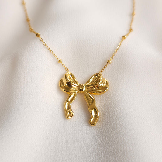 Gold Ribbon Necklace with a sculpted bow pendant and small beads spaced along a fine chain.