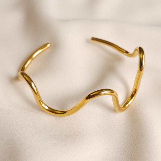 Gold Wave Bangle with flowing curves, a smooth polished finish and an open-ended cuff design.
