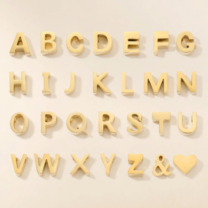 Initial Letter Necklace charm selection showing gold-tone letters A to Z, an ampersand, and a heart arranged in four rows.