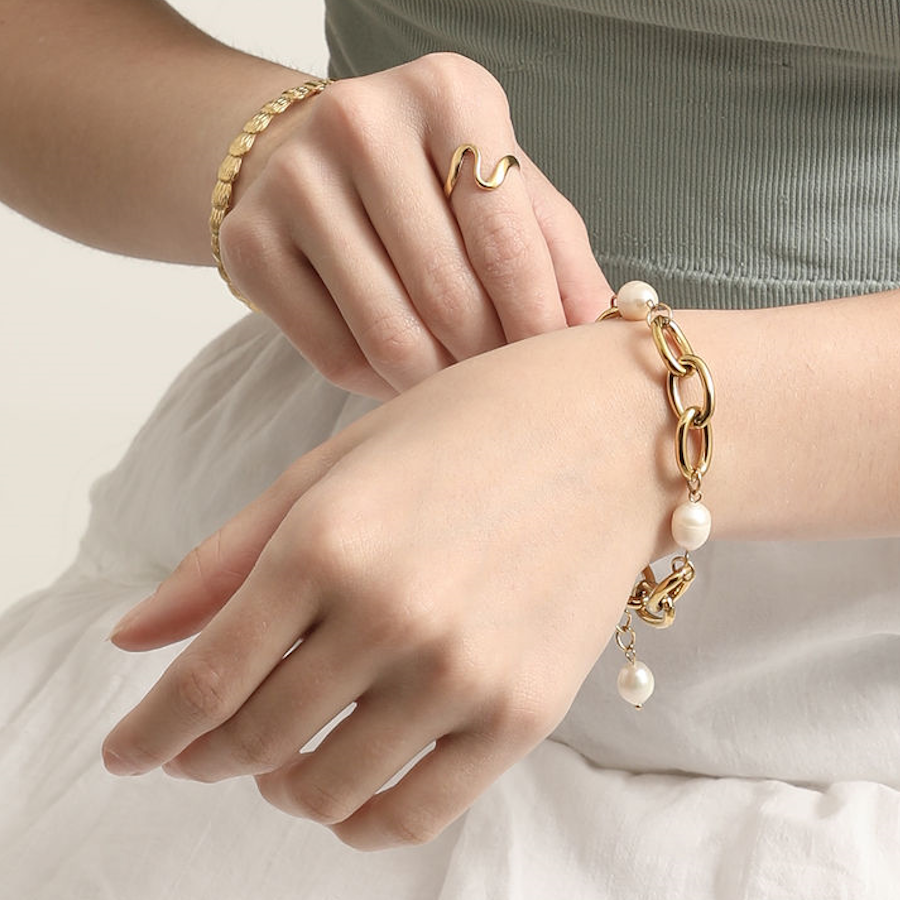 Model wearing the gold Wavy Minimalist Ring alongside the Bold Pearl Chain Bracelet and a gold disc bracelet.
