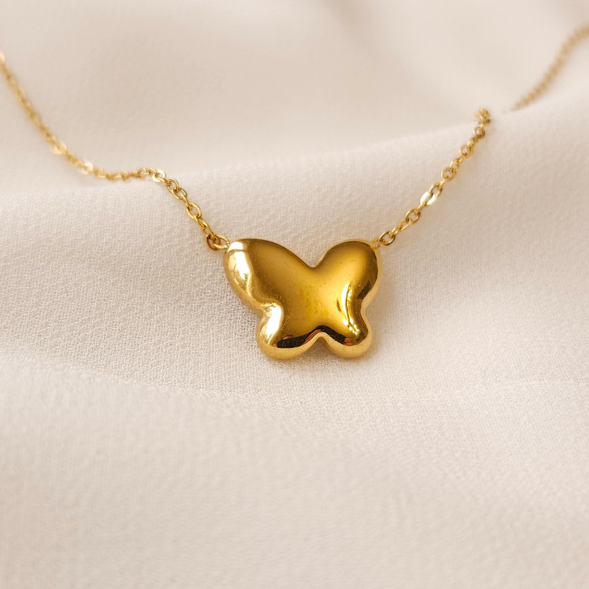 Reverse view of the Mother of Pearl butterfly pendant showing its smooth gold back and fine chain.
