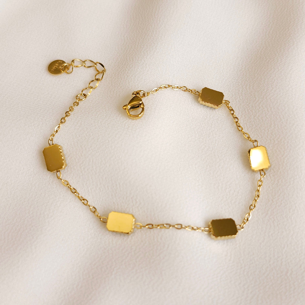 Reverse view of the Satellite Emerald Bracelet showing smooth gold setting backs, a lobster clasp and extension chain.
