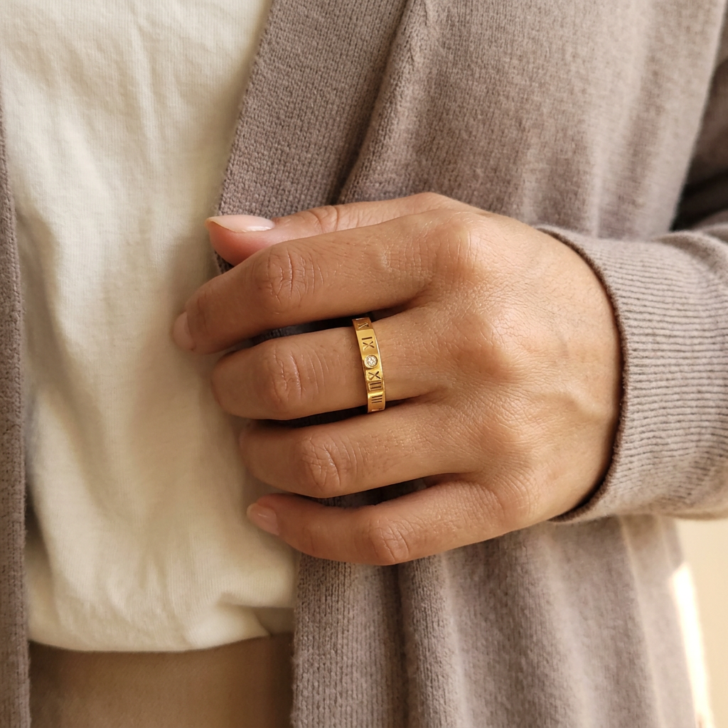 Roman Numeral Band Ring worn on a hand resting against a taupe cardigan, showing the gold-tone band and numeral details.