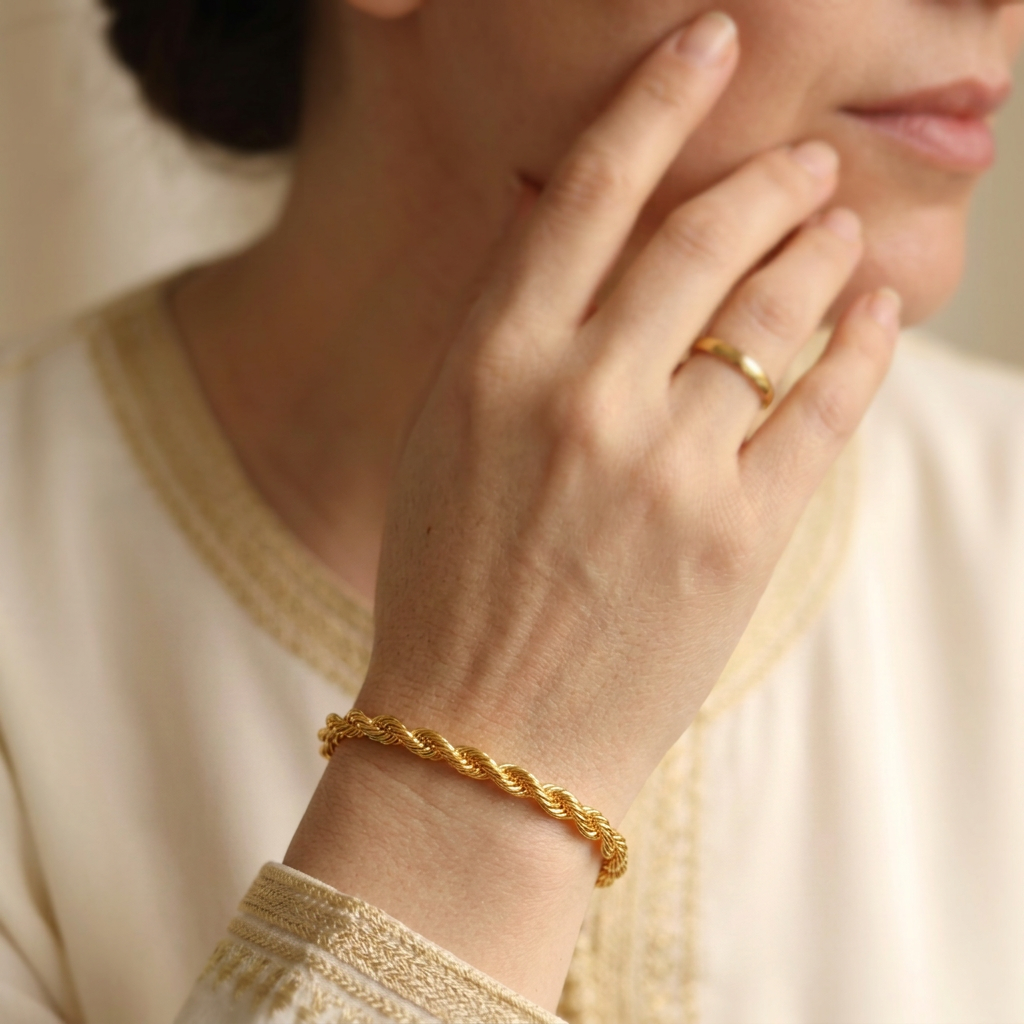 Rope Bracelet worn with a plain gold-tone band ring, with the hand resting near the model’s cheek.