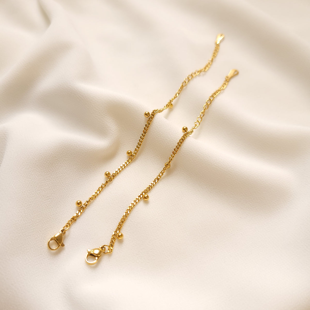 Two gold-tone dangling dots bracelets laid side by side, showing their ball charms, lobster clasps, and extension chains.