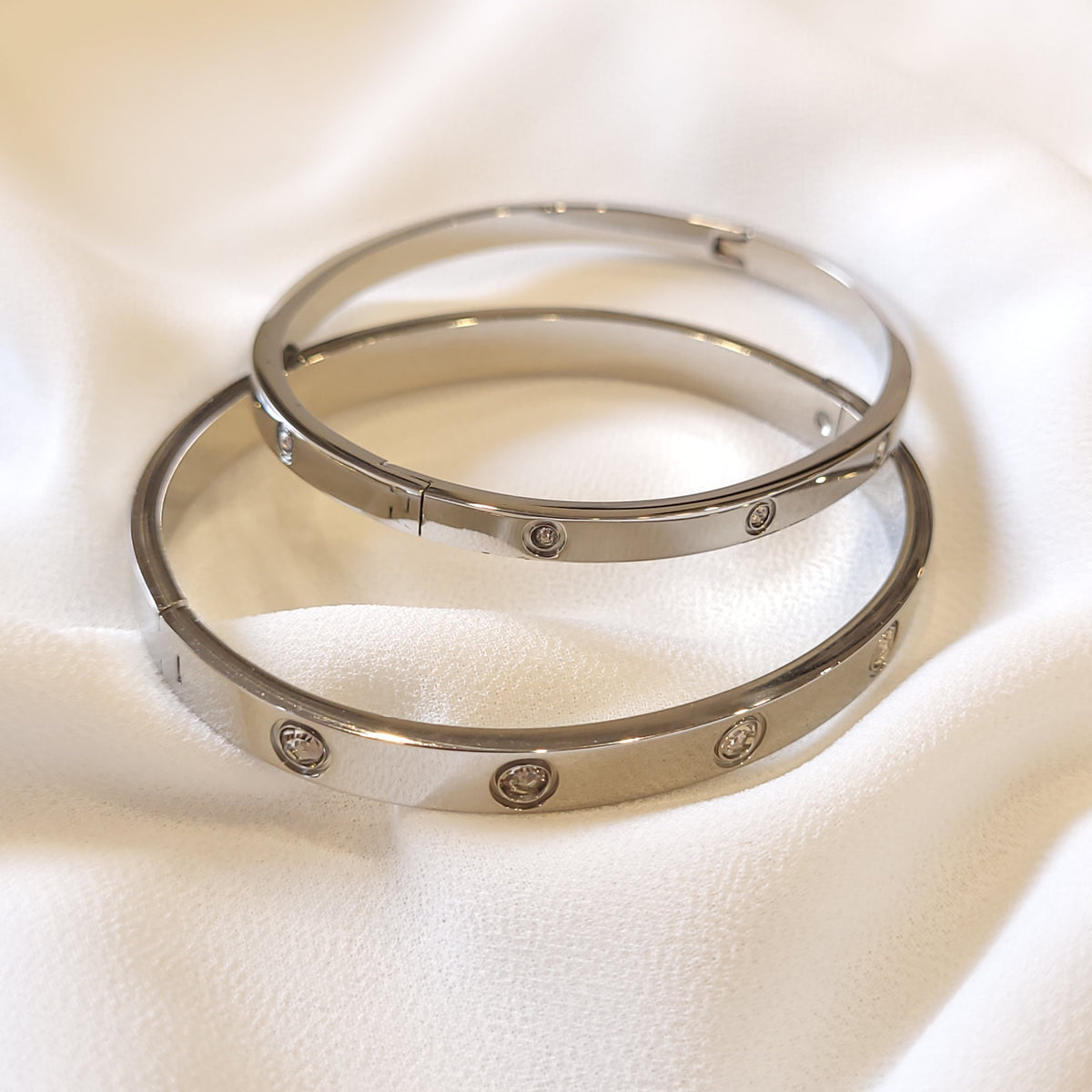 Two silver-tone Crystal Stud Bangles with narrow and wide bands and round clear stones.
