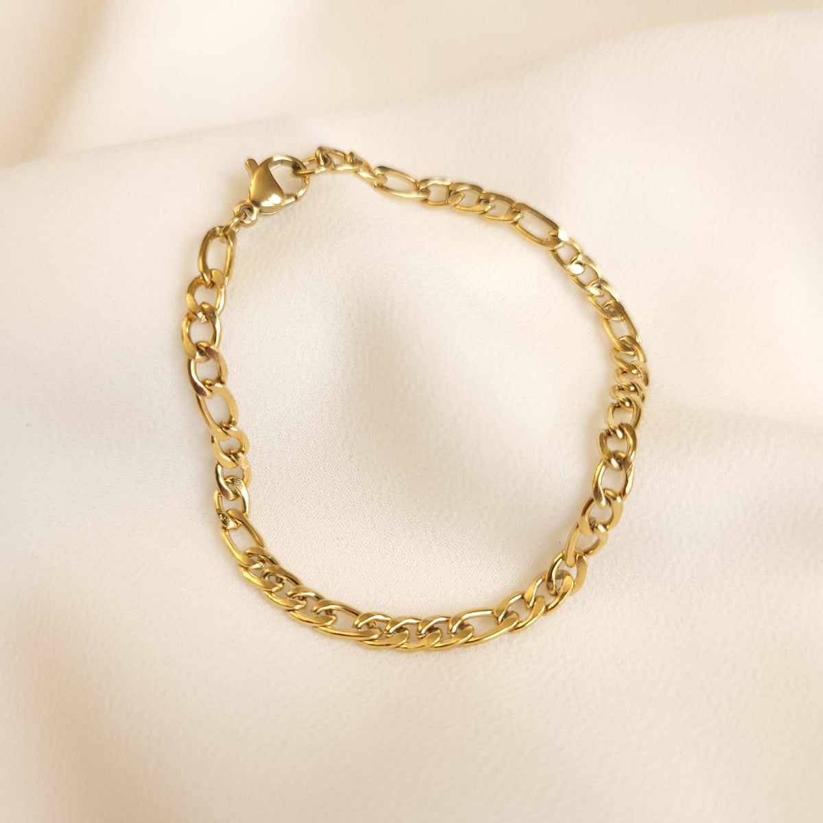 Gold Figaro bracelet arranged in a circle, showing the link pattern and lobster clasp