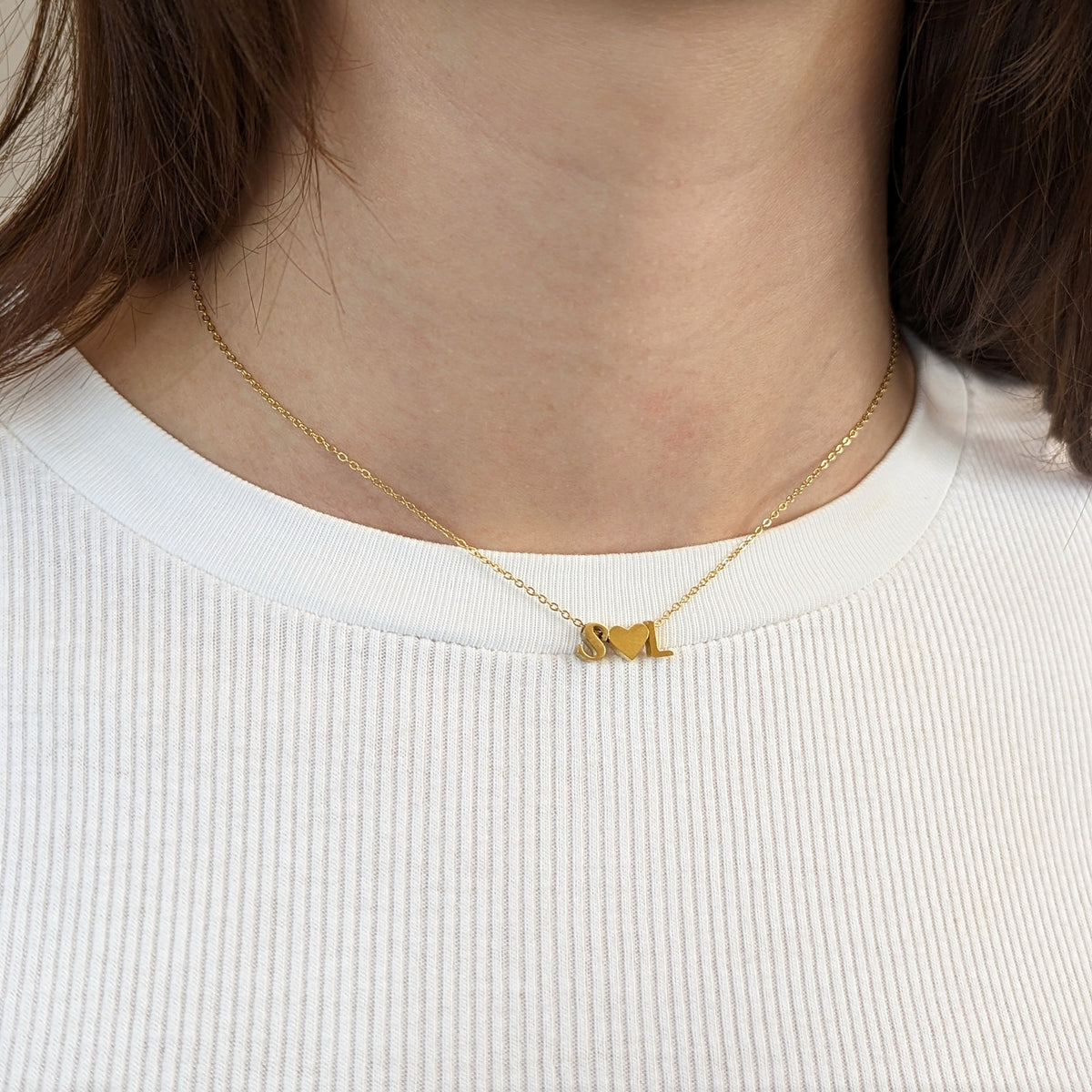 Letter Add-On S and L initials with a heart between them, shown worn at the neckline of a white ribbed top.