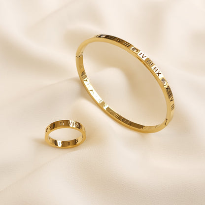 Roman Numeral Bangle displayed upright beside a matching gold-tone ring, both featuring engraved numerals and clear stone accents.