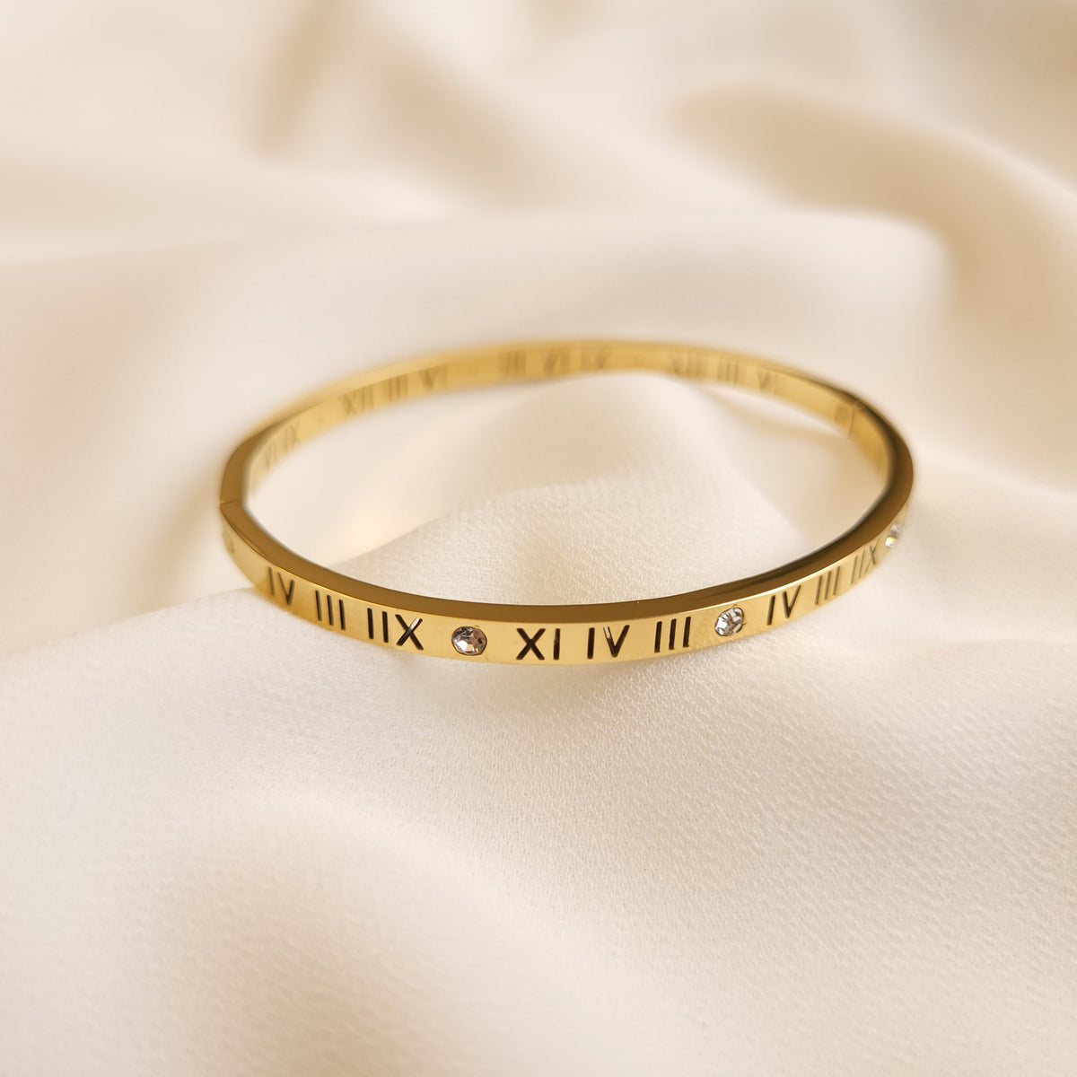 Roman Numeral Bangle in gold tone, featuring black engraved numerals and round clear stone accents along the slim band.