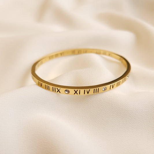 Roman Numeral Bangle in gold tone, featuring black engraved numerals and round clear stone accents along the slim band.