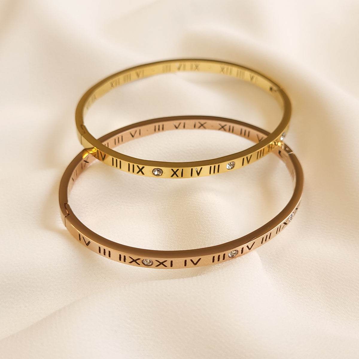 Roman Numeral Bangles in gold and rose gold tones overlapped to compare their finishes, engraved numerals, and clear stone accents.