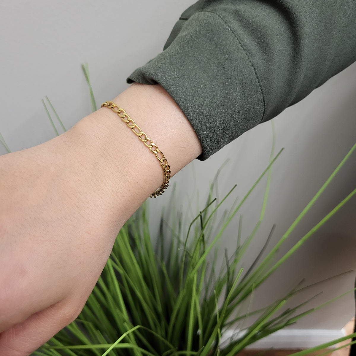 Slim gold Figaro bracelet worn alone on a model’s wrist.