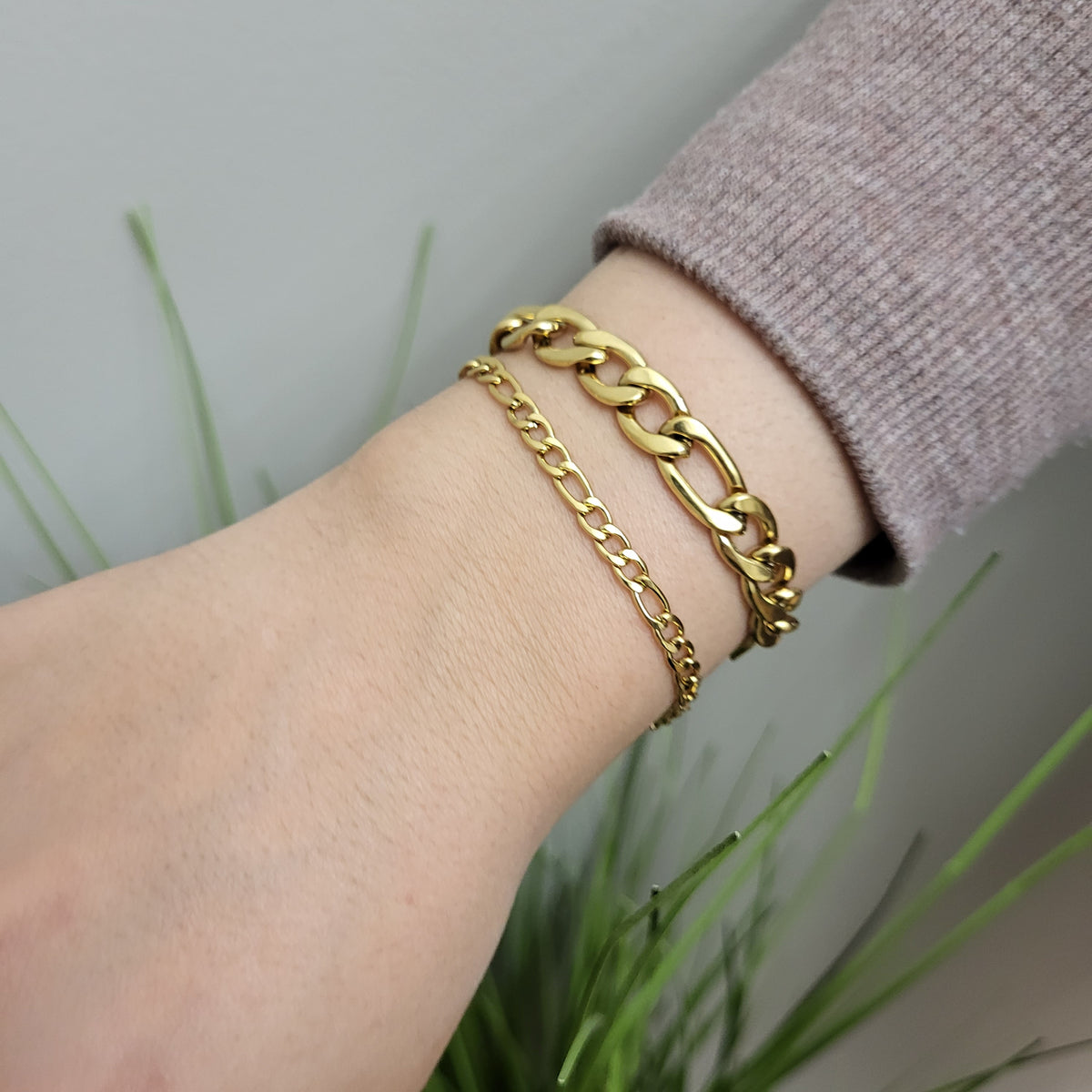 Slim gold Figaro bracelet worn alongside a wider gold Figaro bracelet