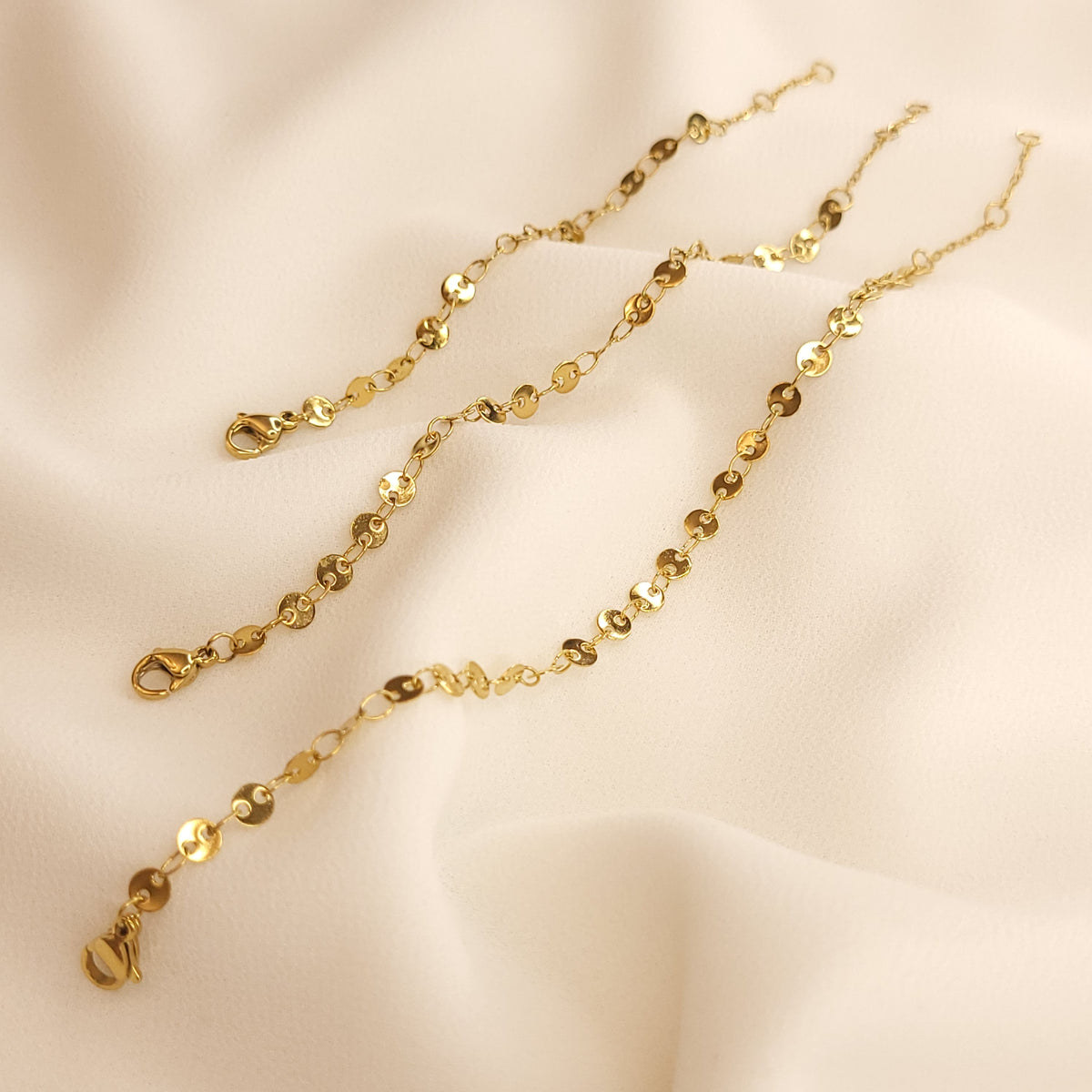 Three gold-tone coin bracelets laid side by side, showing their different lengths, linked discs, and lobster clasps